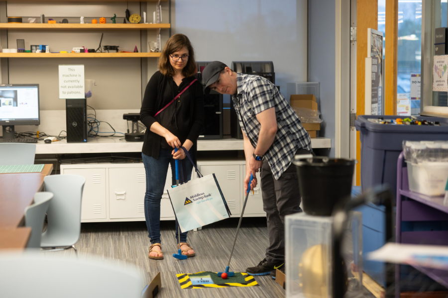 Two people playing mini golf in the library.