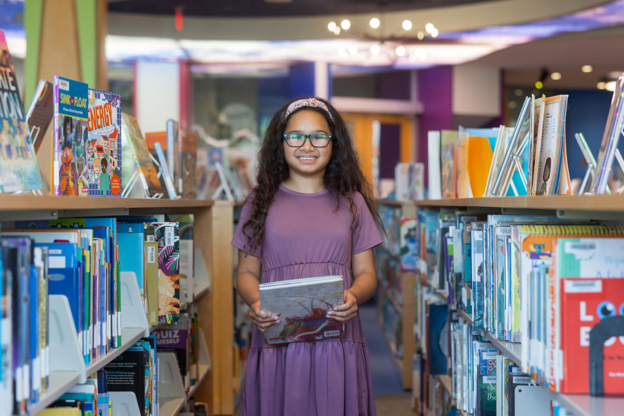 A child in the children's room picking out a book, points to Kid's page.