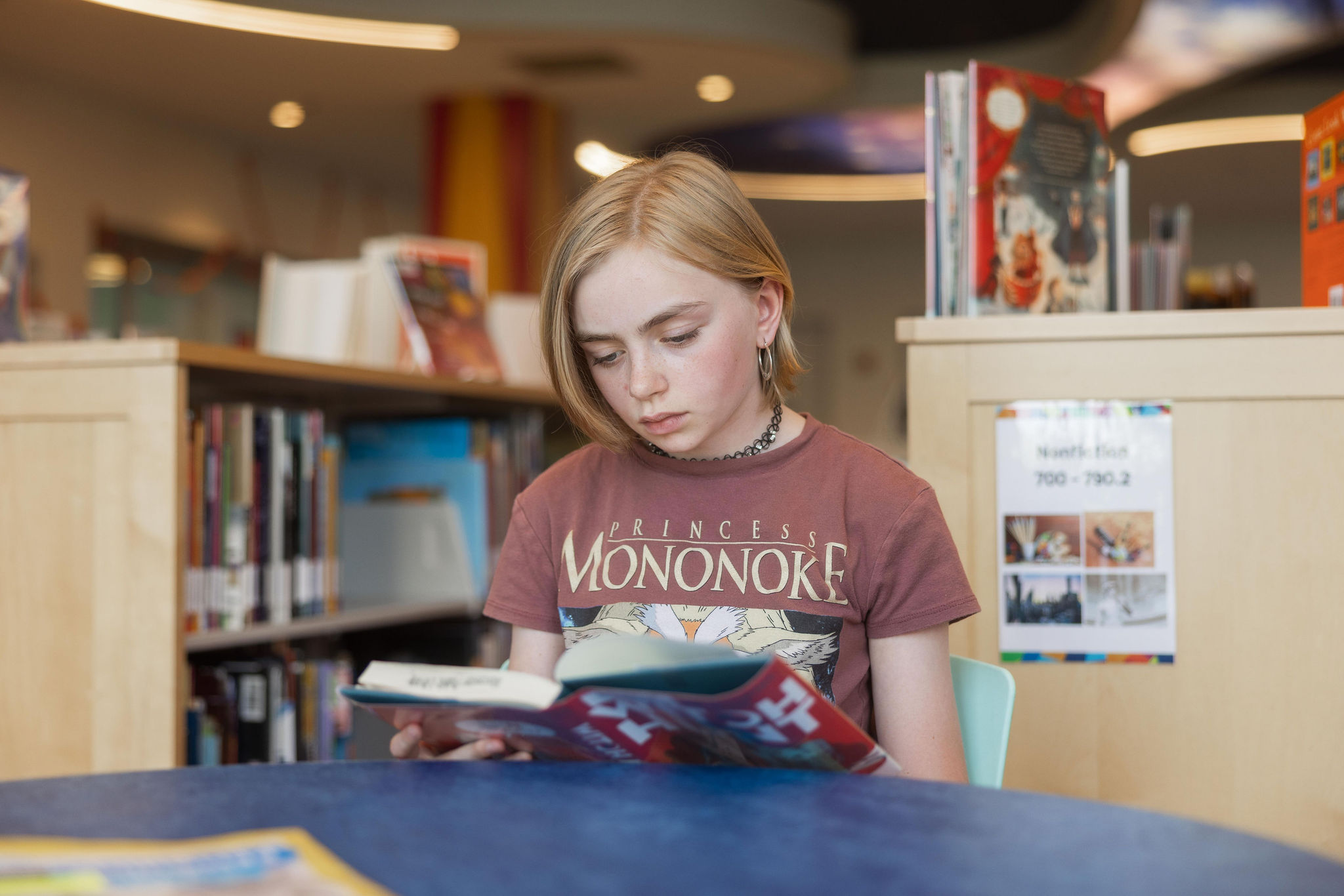 Tween in the library reading a book, points to Tween page.