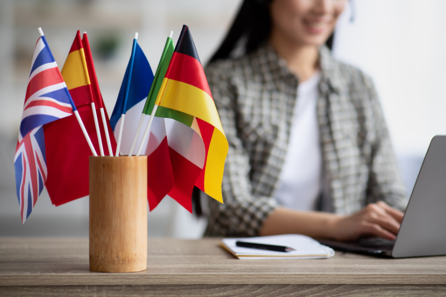 A woman works on a laptop with a vase of different country flags in the foreground.