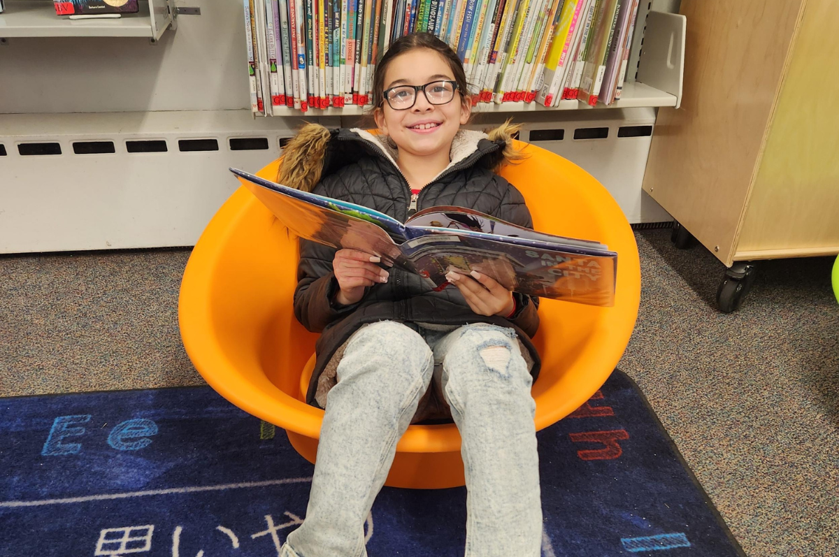 Teen sitting in chair reading a book, points to teen page.